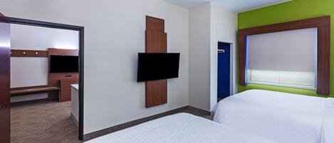 Una habitación de hotel con una cama grande, un televisor de pantalla plana en la pared, un escritorio con una silla y una puerta con marco azul.