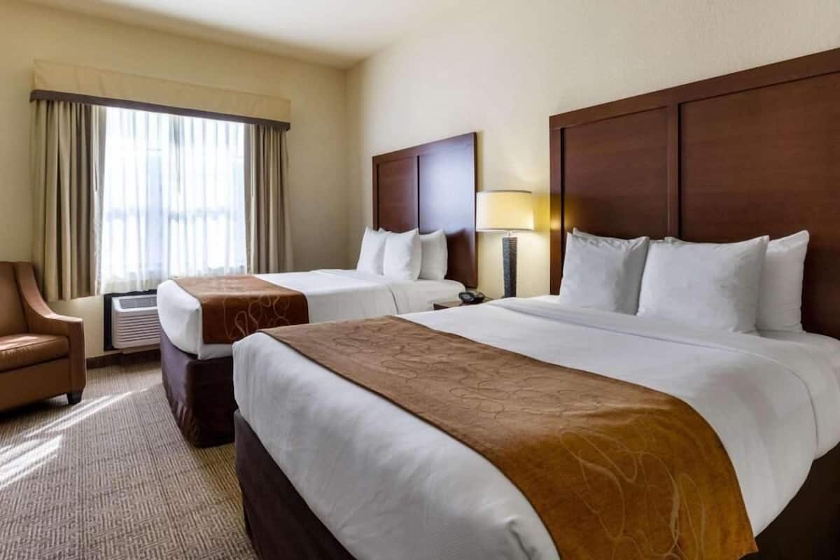 A hotel room with two beds, a chair, a lamp, and a window with curtains.