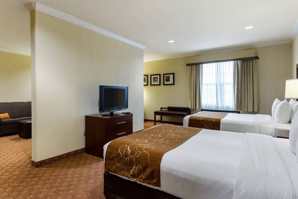 A hotel room with two beds, a TV on a dresser, a desk, and a window with curtains.