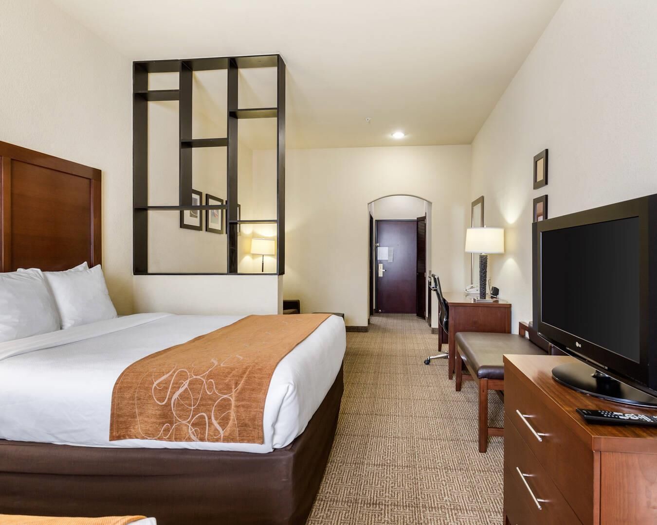 A hotel room with a large bed, a TV, a desk, and a mirror.