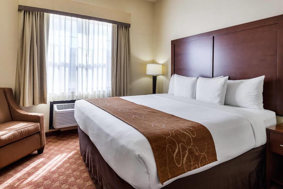 A hotel room with a large bed, a chair, a lamp, and a window with curtains.