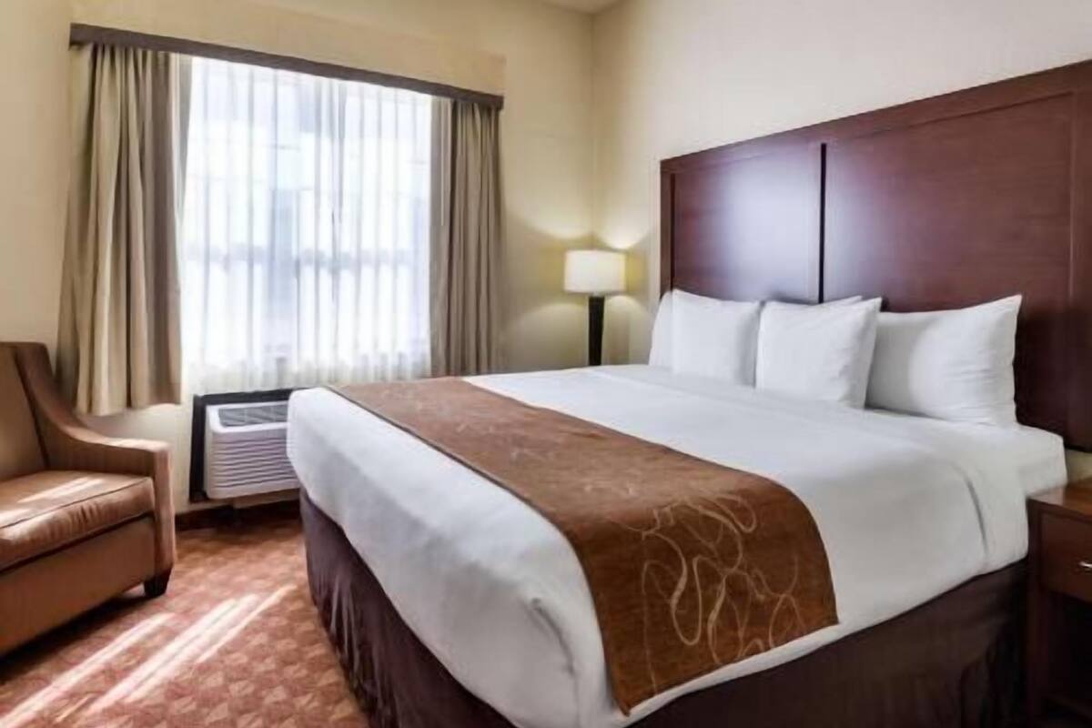 A hotel room with a bed, a chair, a lamp, and a window with curtains.