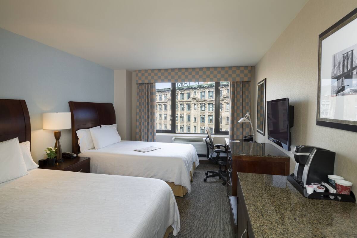 Una habitación de hotel con dos camas, un escritorio con computadora, cafetera y televisión.