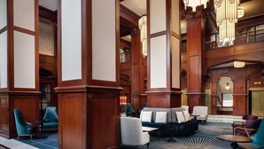 Eine geräumige Lobby mit hohen Holzsäulen, einer zentralen Sitzgruppe mit Sofas und Sesseln sowie einem gemusterten Boden.
