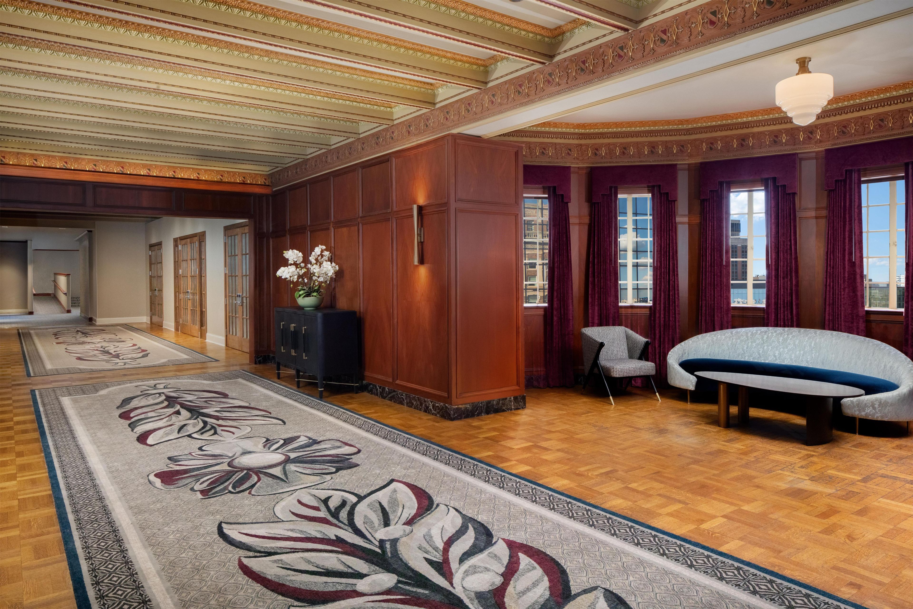 A spacious lobby with a high ceiling, wooden paneling, a large floral rug, a sofa, and a chair.