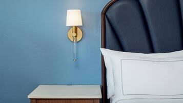 A bedroom with a blue wall, a bedside table, a lamp, and a bed with white bedding.