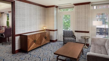 A hotel room with a wooden console table, patterned carpet, a sofa, and a chair.