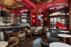 Zona de bar con diferentes opciones de asientos, incluyendo cabinas y mesas, un piano y una barra con una selección de botellas.