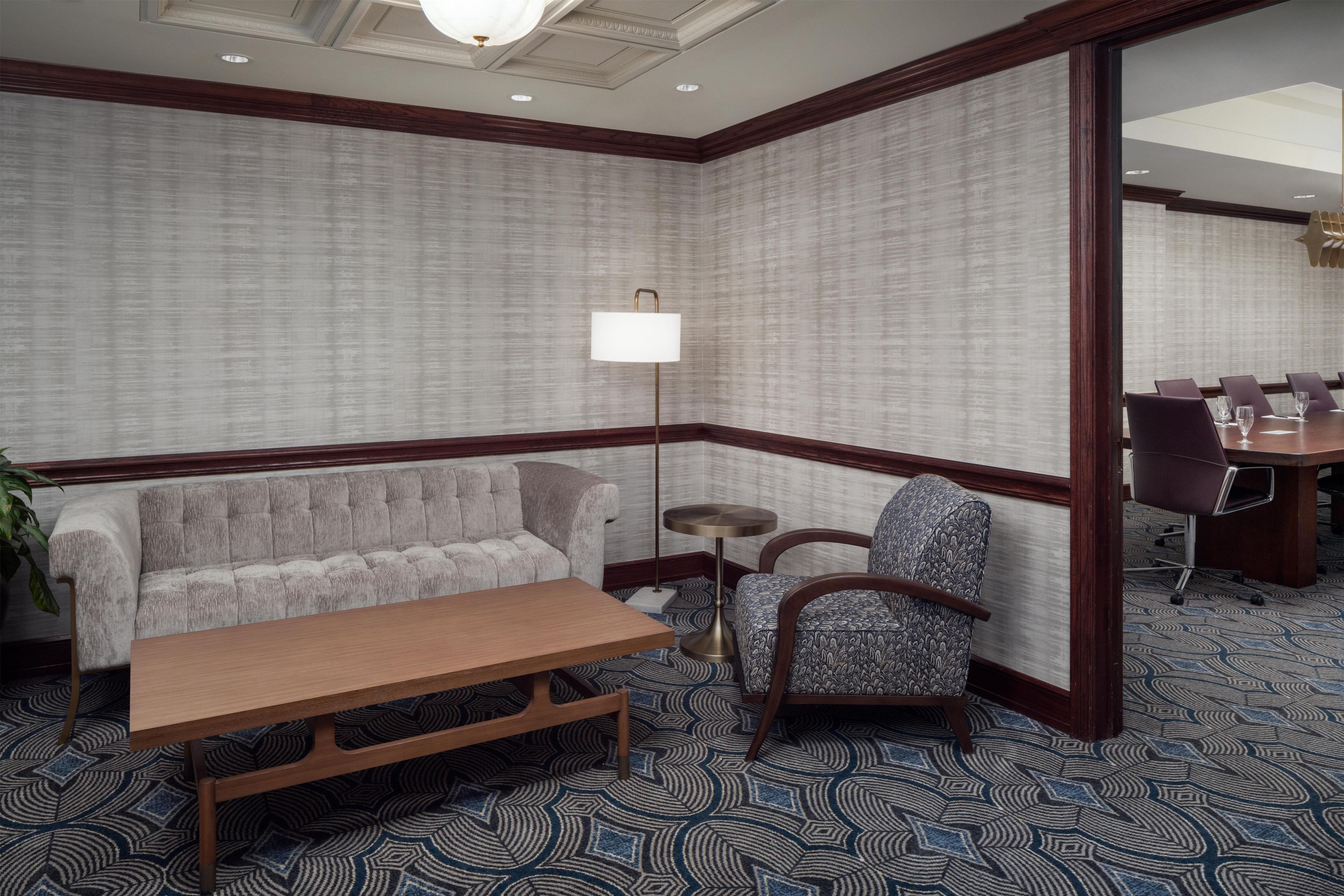 A hotel room with a sofa, a chair, a small table, and a lamp.