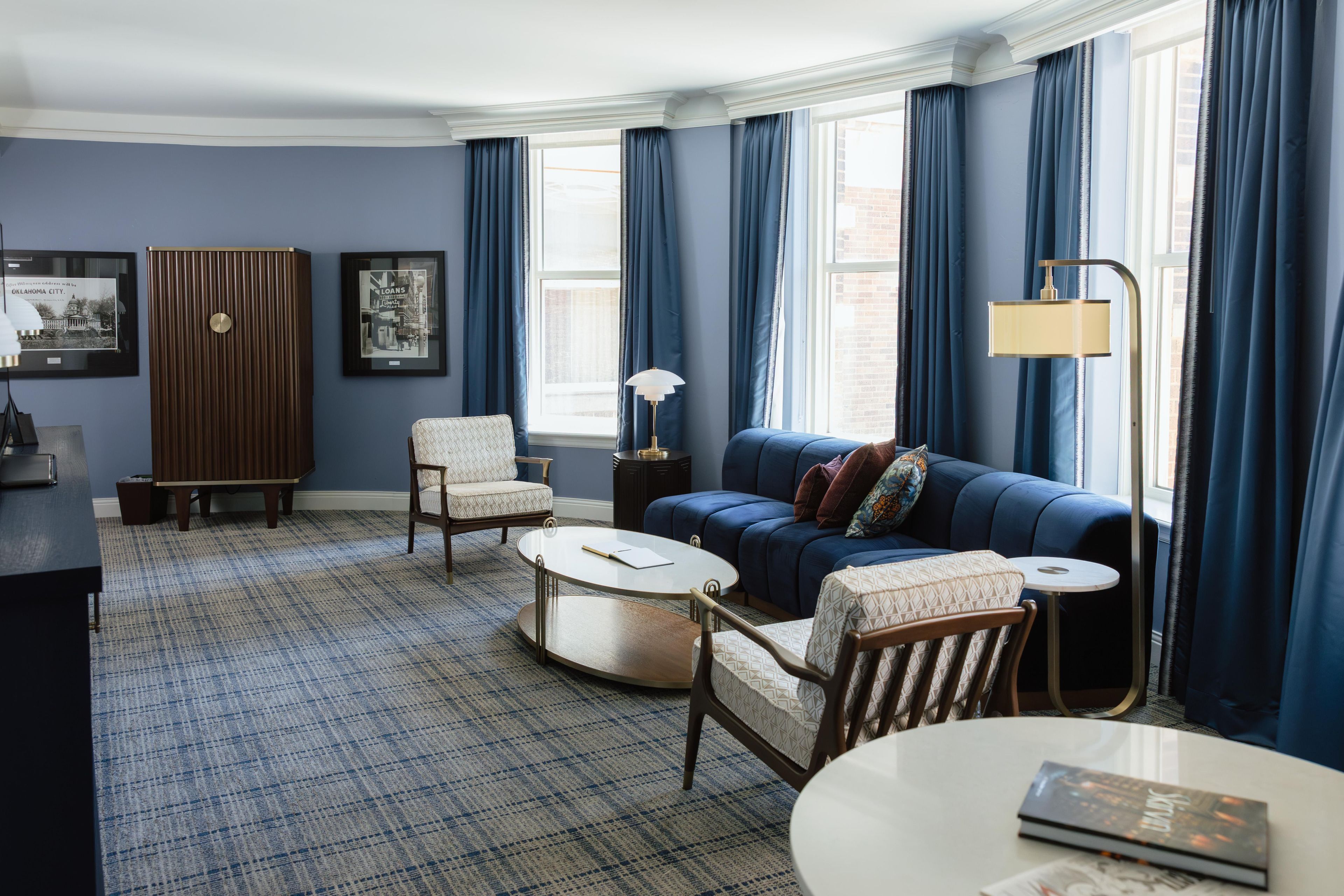 Una habitación con un sofá azul, dos sillones, una mesita de centro, una lámpara y cuadros enmarcados en la pared.