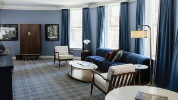 Una habitación con un sofá azul, dos sillones, una mesita de centro, una lámpara y cuadros enmarcados en la pared.