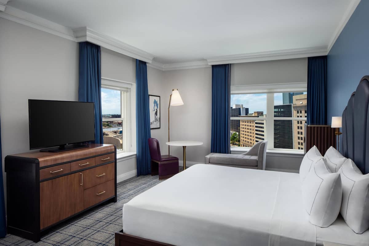 Ein Hotelzimmer mit einem großen Bett, einem Fernseher auf einer Holzkommode, einem kleinen Tisch und einem Stuhl.