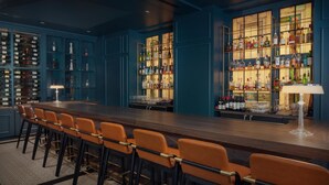 Eine Bar mit einer langen Holztheke, mehreren Flaschenregalen und orangefarbenen Barhocker.