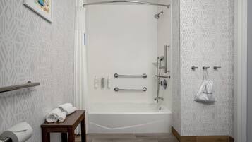 A modern bathroom with a bathtub, shower, and handrails. There is a towel rack and a small table with towels.