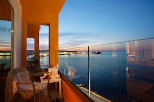 Ein Balkon mit Blick auf ein Gewässer und Stadtlichter in der Dämmerung.