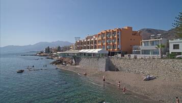 Un hotel en la costa con aguas azules cristalinas, un muro de piedra y una playa.