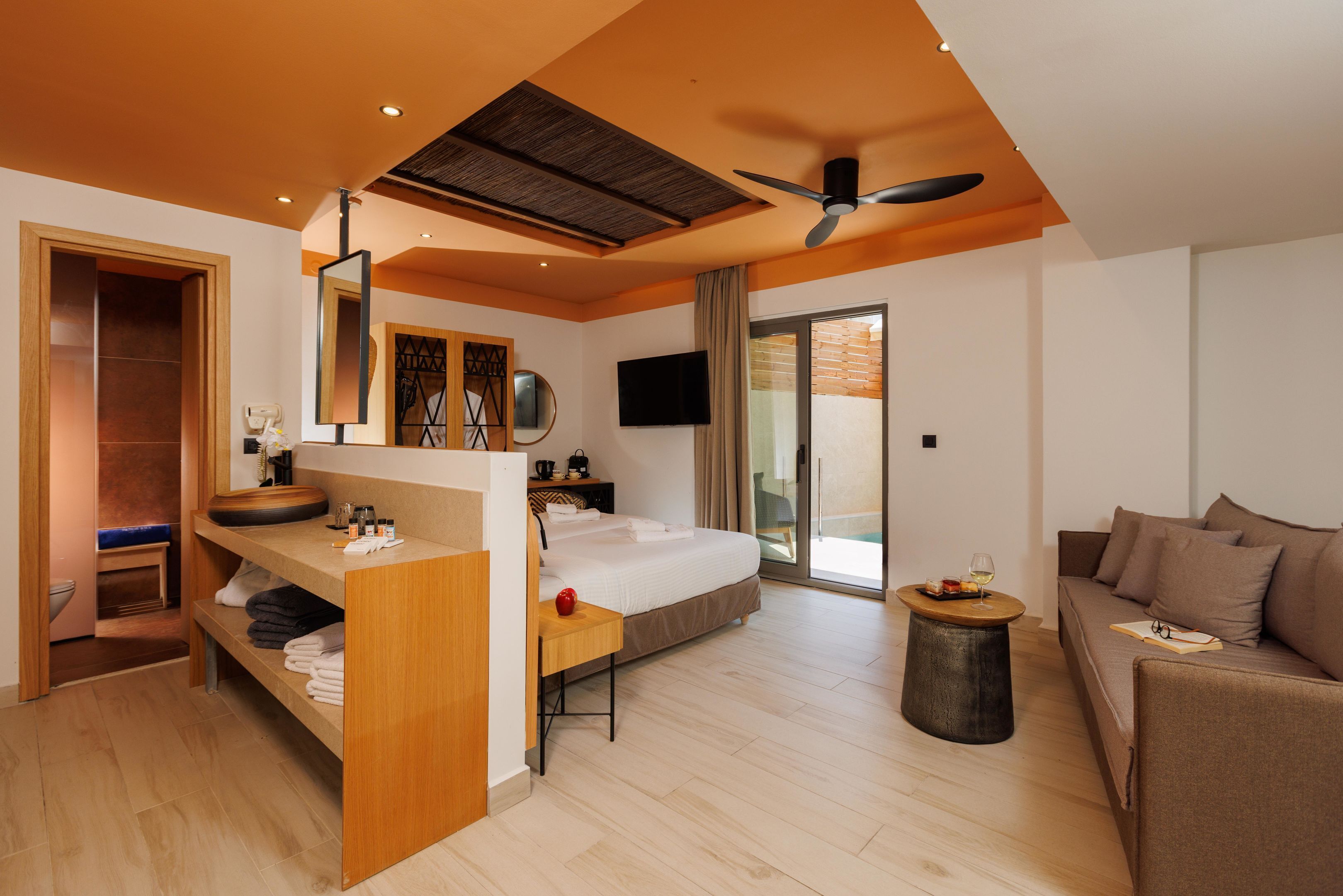 Una habitación de hotel moderna con una cama, un escritorio de madera, una mesa redonda para café, un sofá y un televisor.
