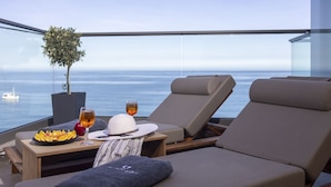 Un balcón con vista al mar, una mesa con frutas, vasos y un sombrero.