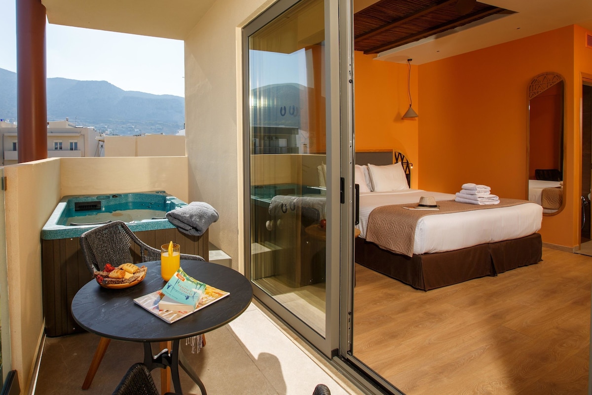 Un balcón con un jacuzzi, una mesa con una carta y una bebida, y un dormitorio con una cama y un ventilador de techo.