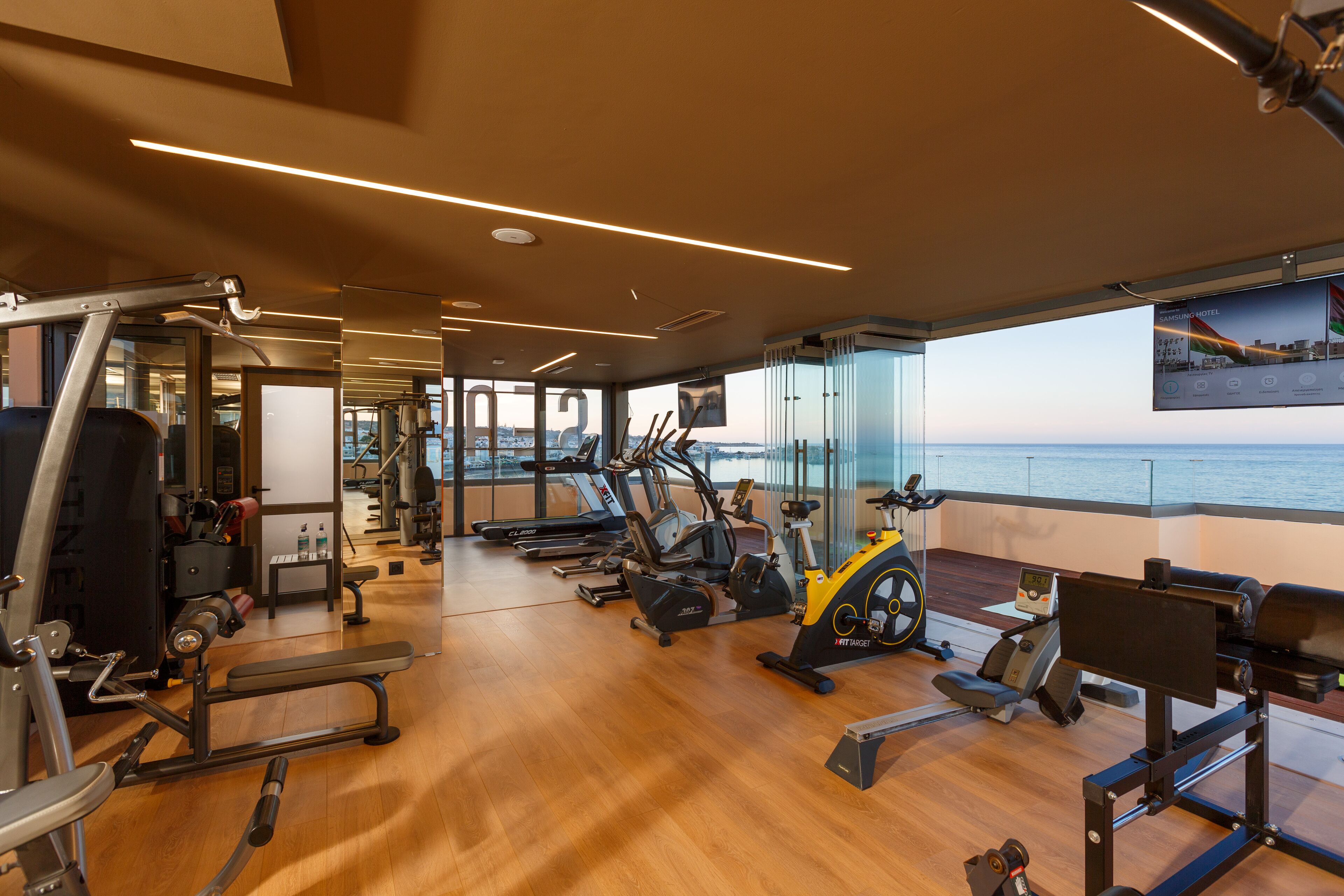 Une salle de sport équipée de divers appareils d’exercice, dotée de grandes fenêtres et offrant une vue sur la mer.