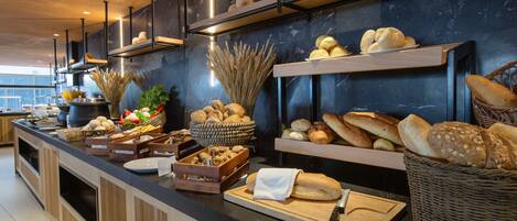 Una mesa de buffet con panes, pasteles y frutas variadas.
