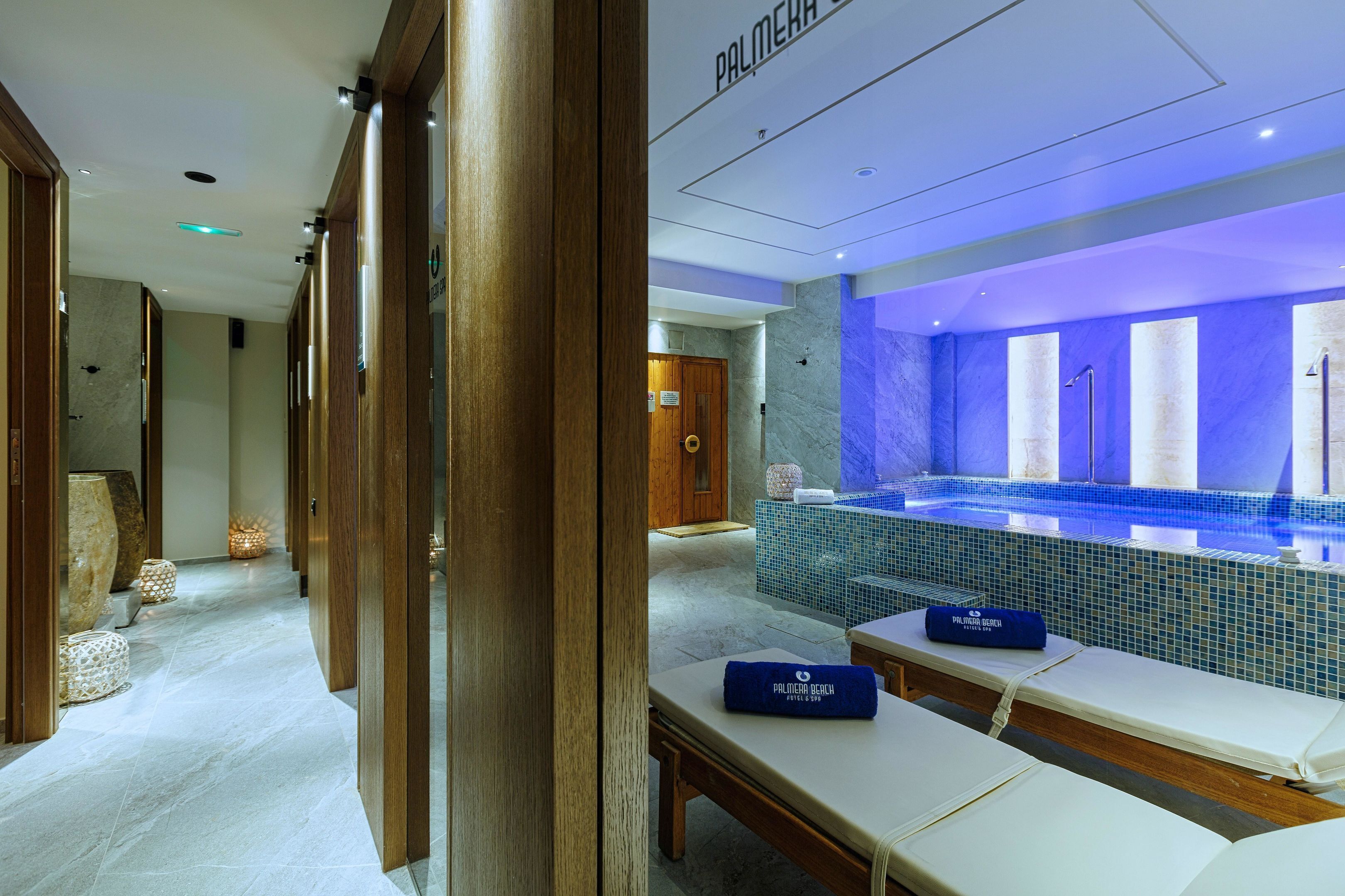 Un área de spa con una amplia piscina de azulejos azules, bancos de madera y un mostrador de recepción.
