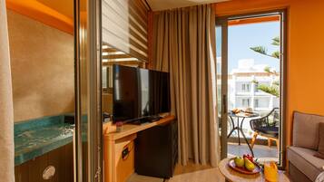 A hotel room with a TV, a small fridge, a balcony with a table and chairs, and a sofa.