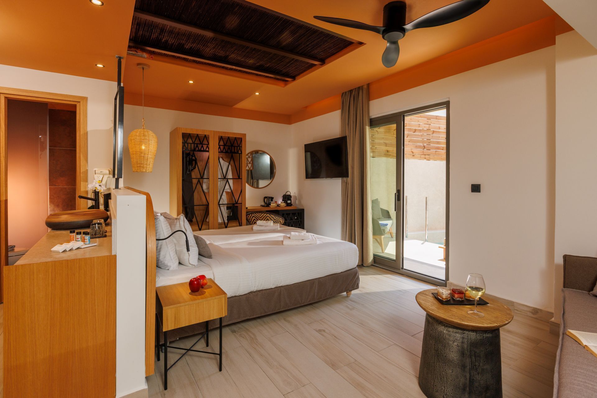A modern hotel room with a large bed, a desk, a small table, and a balcony with a view.