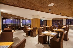 Un restaurante moderno con paneles de techo de madera, sillas tapizadas en marrón y grandes ventanales con vistas a la ciudad.