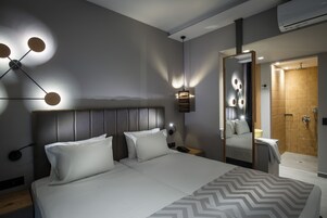 A modern hotel room with a large bed, bedside tables, a nightstand, a wall-mounted lamp, and a shower area.