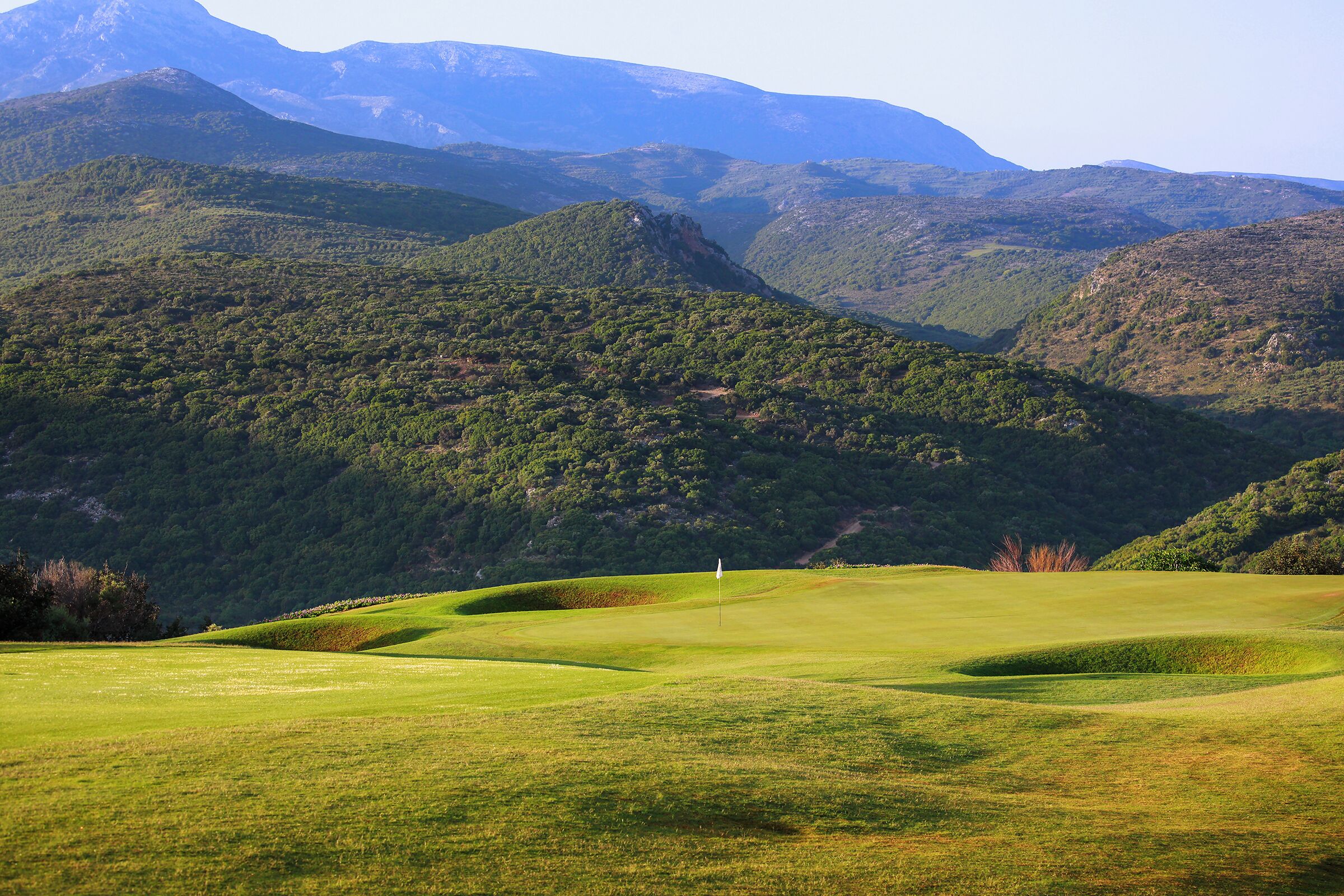 A golf course with rolling hills and mountains in the background.