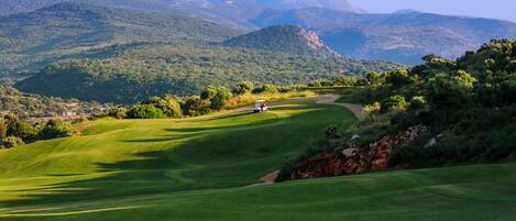 A golf course with rolling green hills and distant mountains.