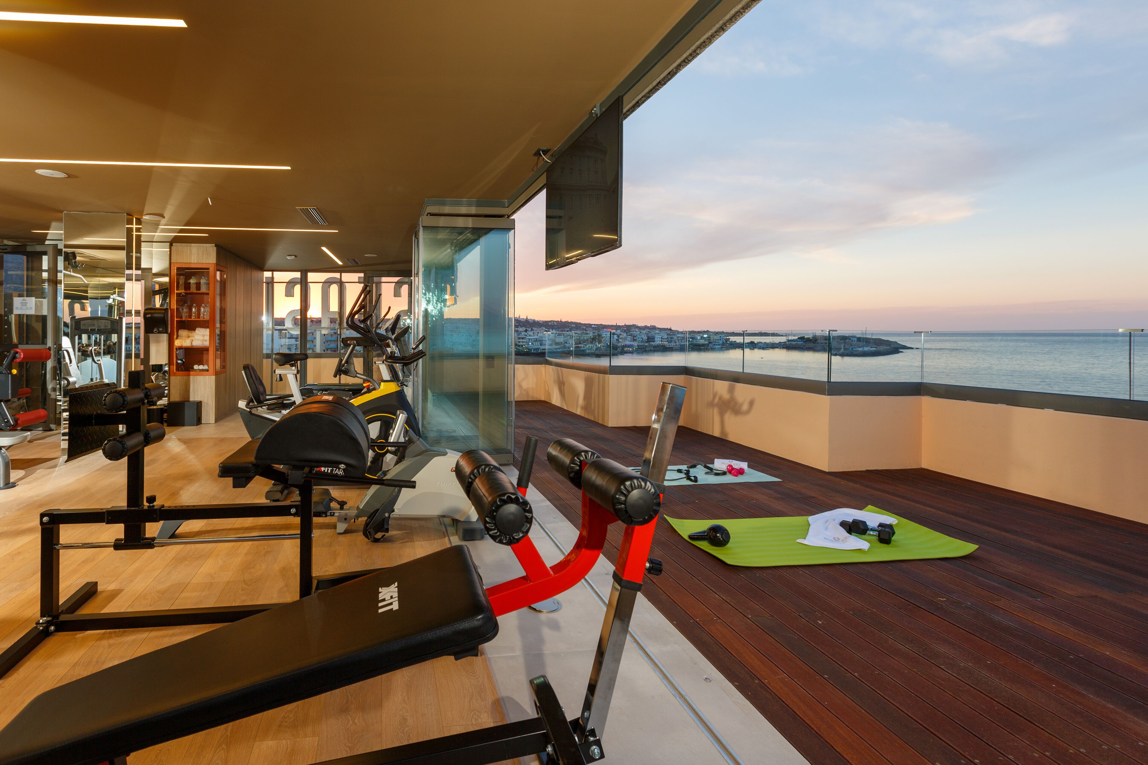 Une salle de sport équipée de matériel d’exercice, offrant une vue sur le paysage urbain et un plan d’eau.
