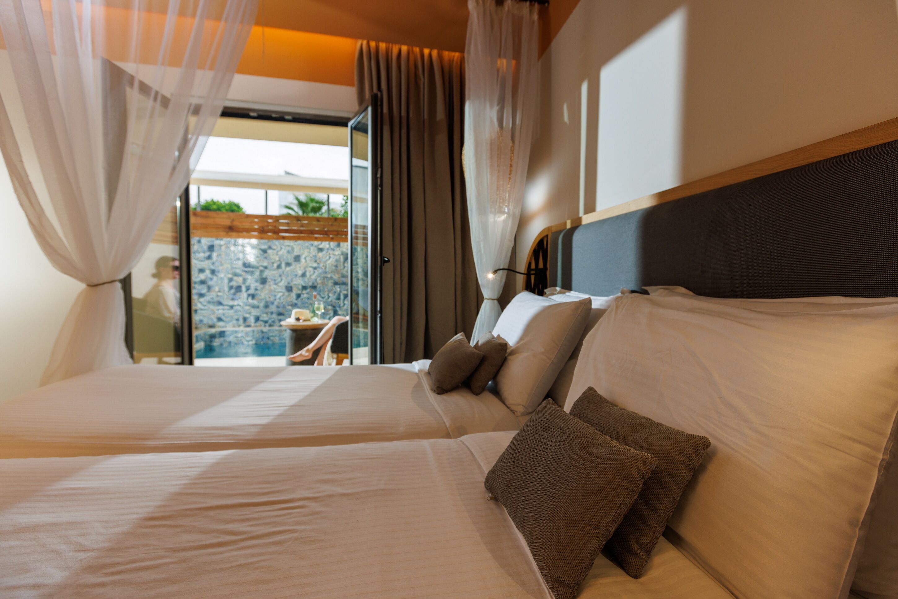 A hotel room with two beds, a balcony with a view, and a dining area visible through the open door.