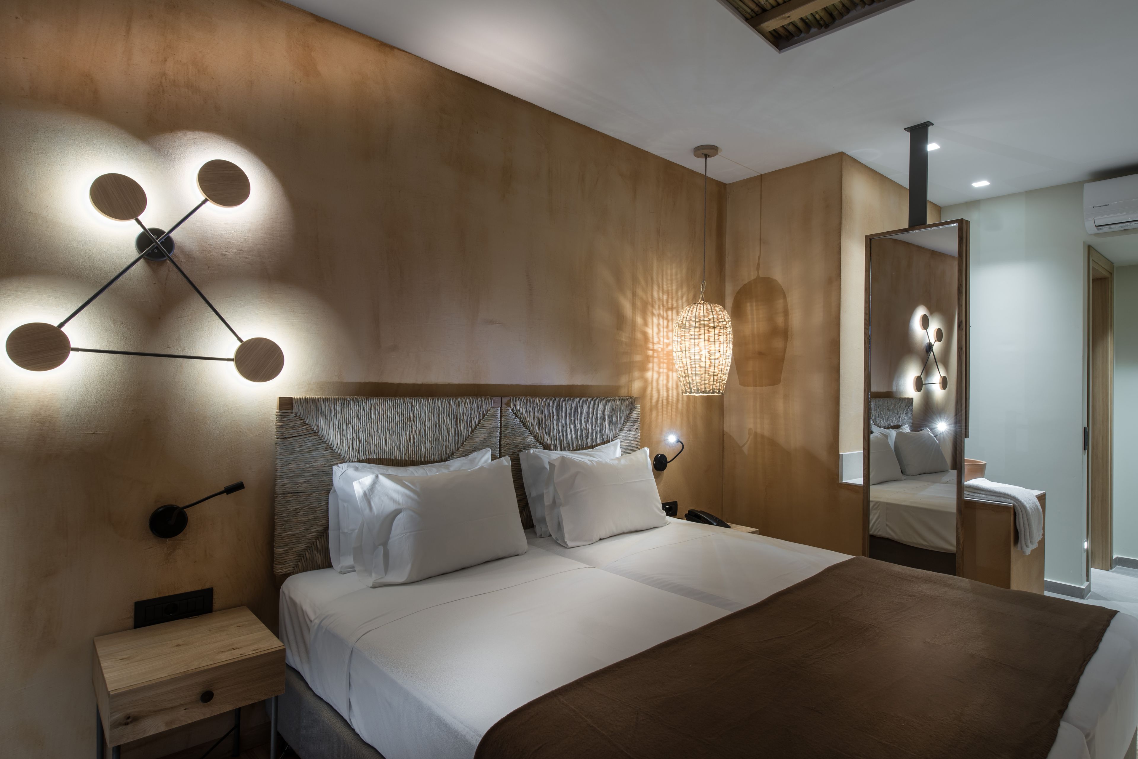 A modern hotel room with a large bed, a wooden headboard, a bedside table, and a wall-mounted light fixture.
