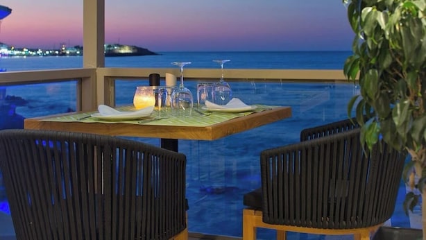 Una mesa de comedor con sillas y vistas al océano al atardecer.