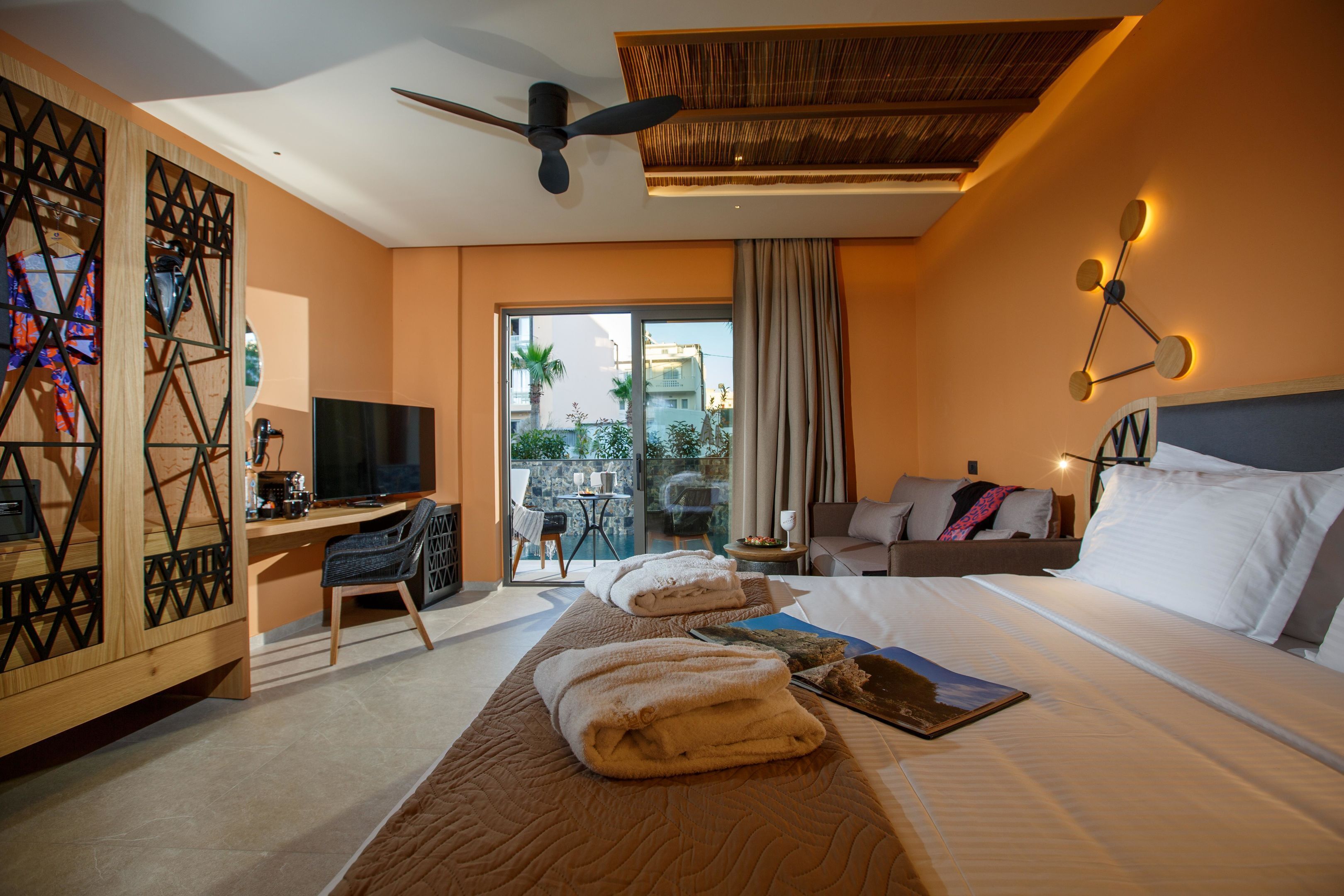 A hotel room with a bed, a desk, a chair, a TV, and a view of the outside.