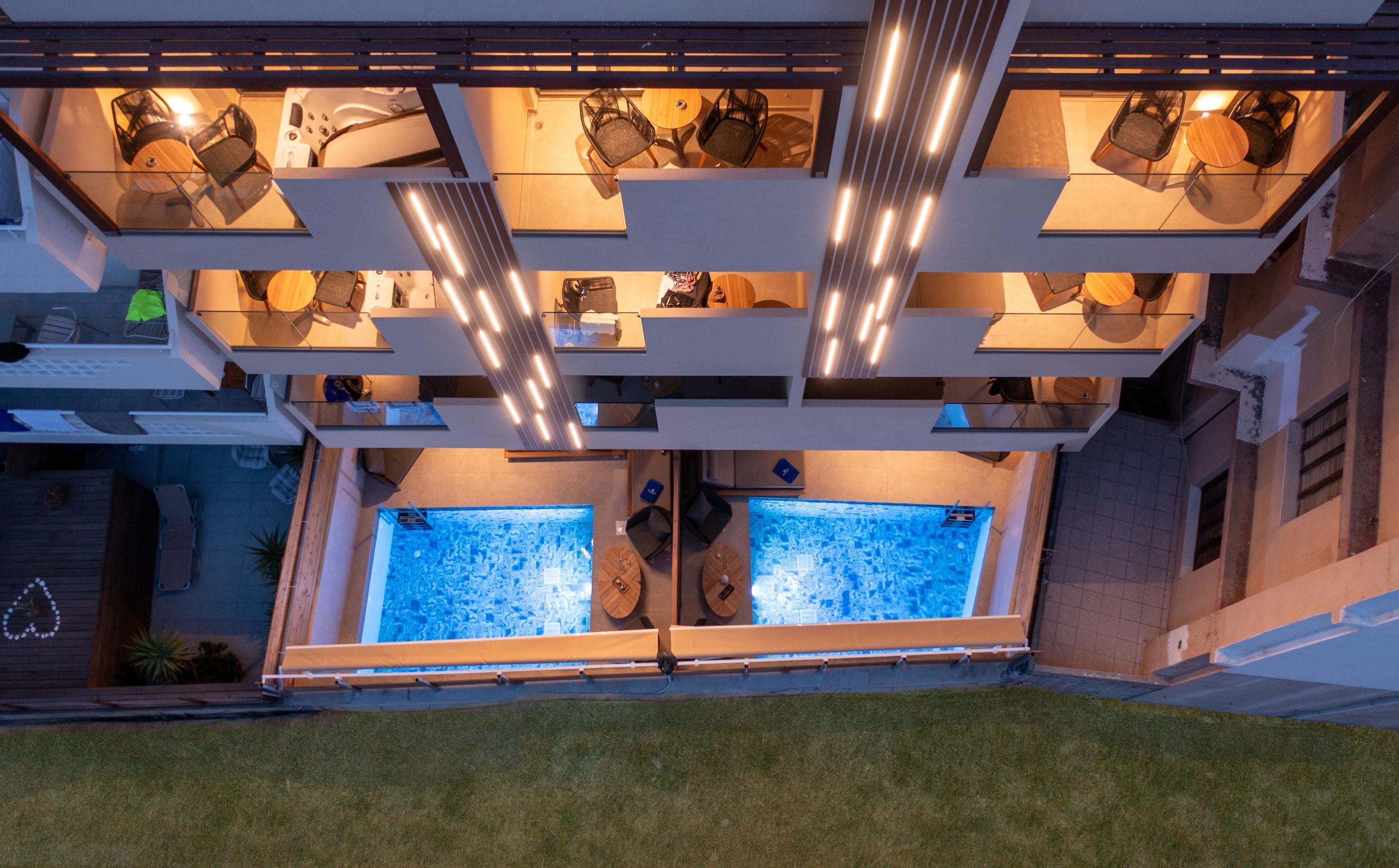 Un área de piscina exterior moderna con dos jacuzzis, rodeada por un espacio de estar techado con sillas y mesas.