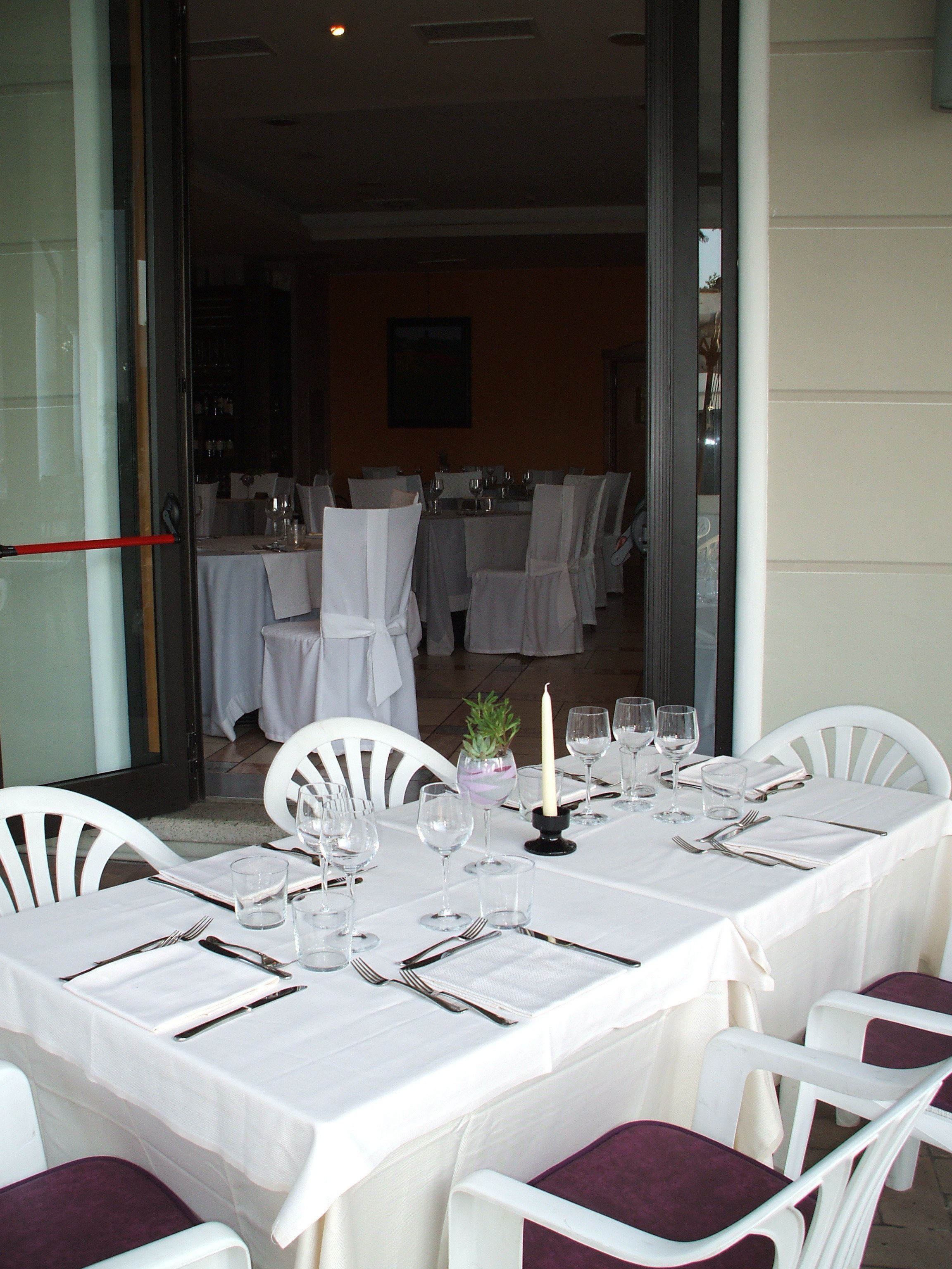 A dining area with tables set for a meal, chairs, and a candle centerpiece.