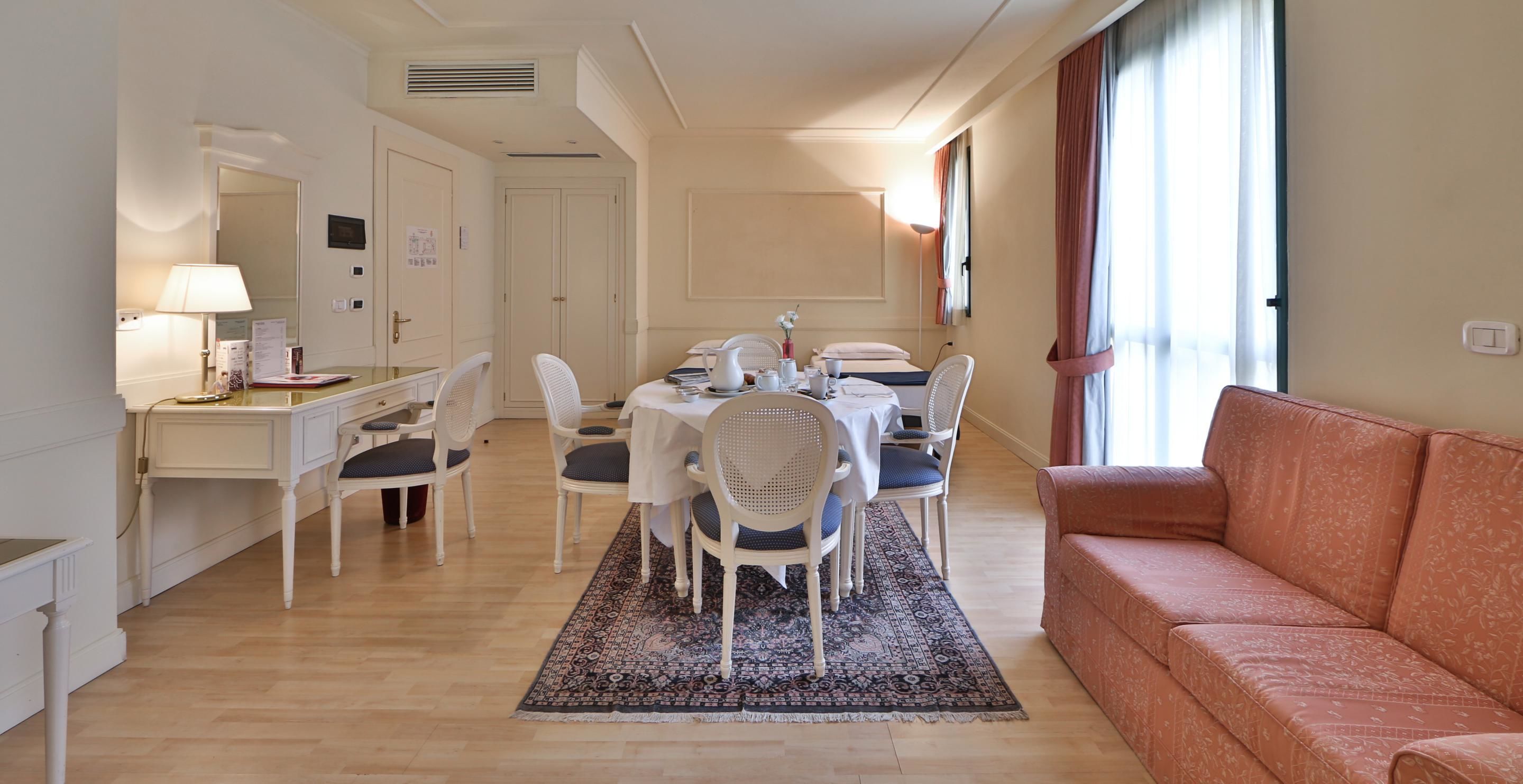 Una camera d'albergo con zona pranzo, divano, scrivania e lampada.