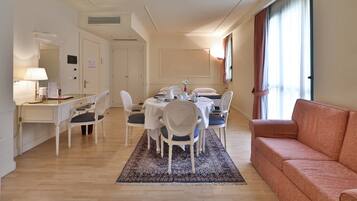Una camera d'albergo con zona pranzo, divano, scrivania e lampada.