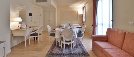 A hotel room with a dining area, a sofa, a desk, and a lamp.