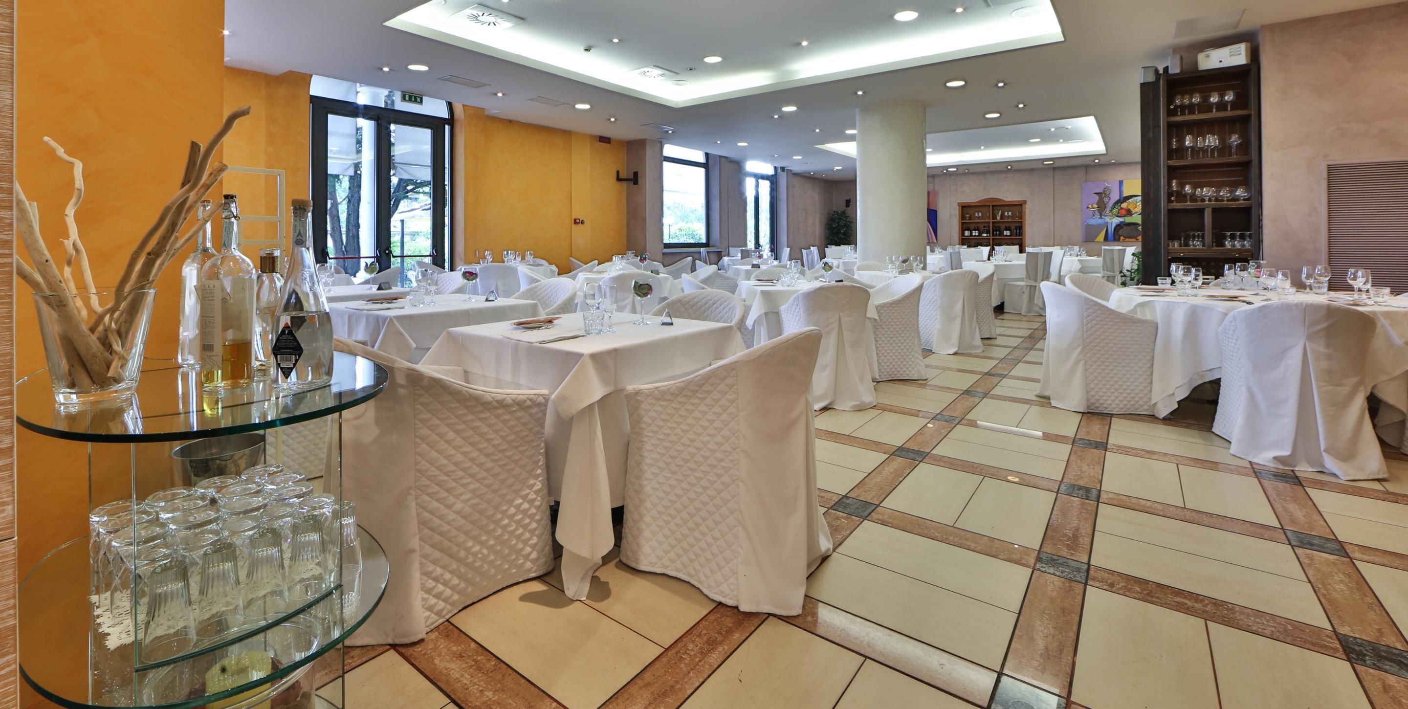 A spacious dining area with round tables covered in white tablecloths, glassware, and cutlery.