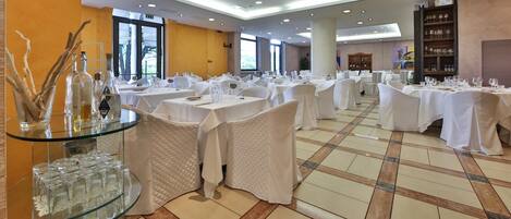 A spacious dining area with round tables covered in white tablecloths, glassware, and cutlery.