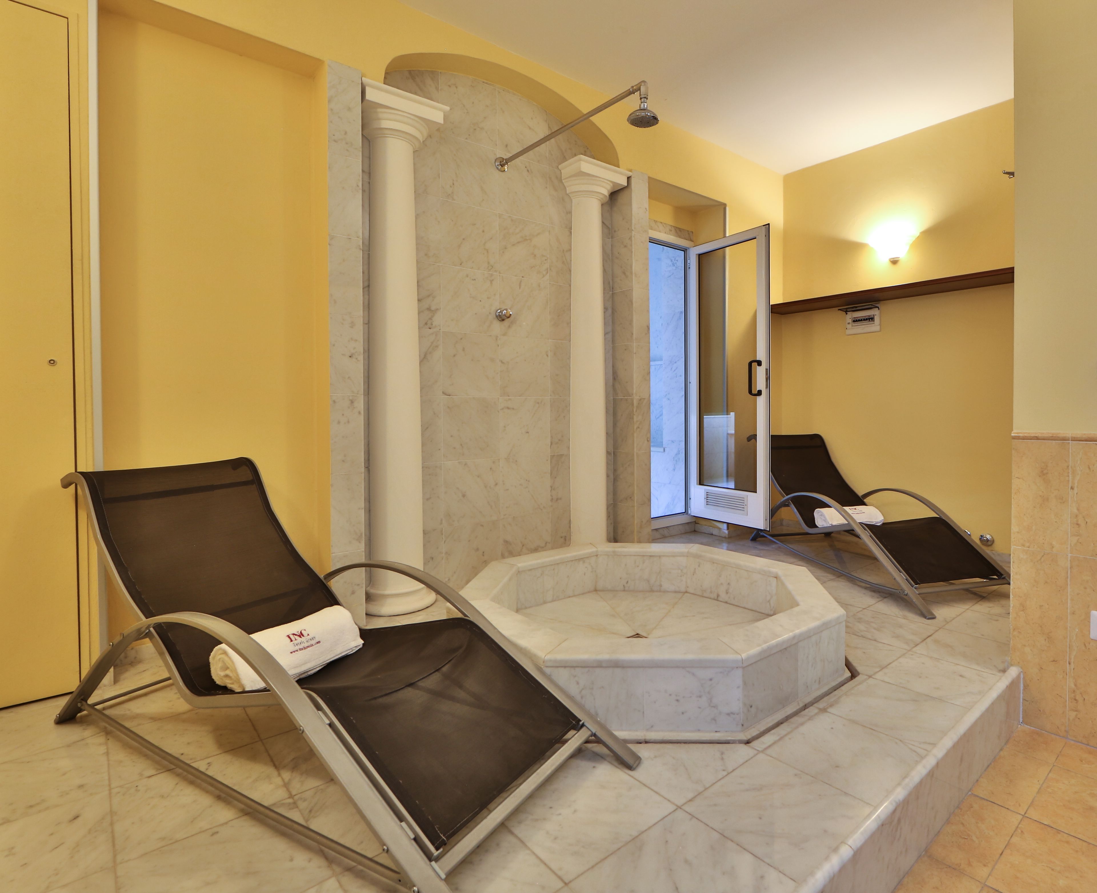 A spa area with two reclining chairs, a marble hot tub, and a shower with a glass door.