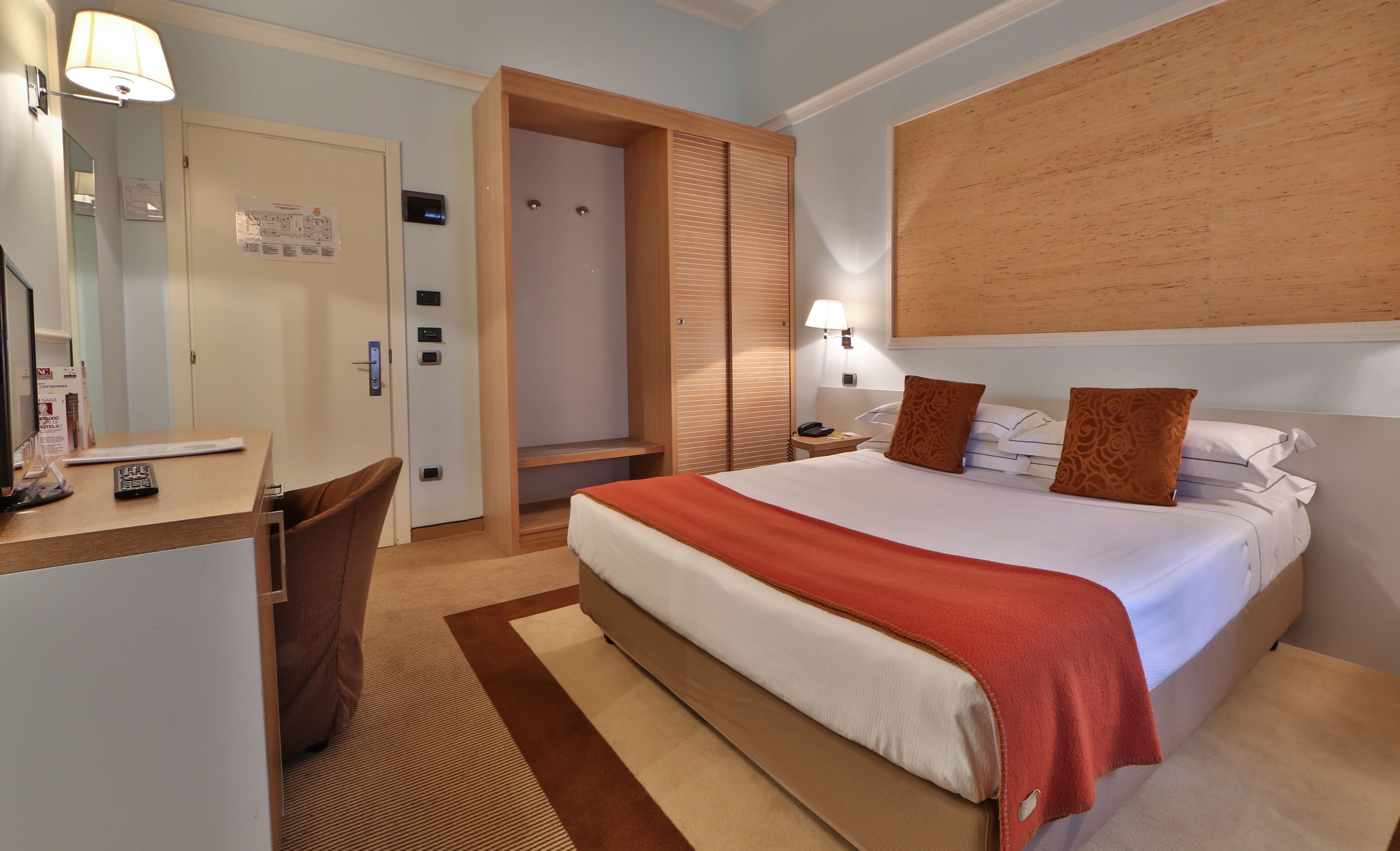Una habitación de hotel con cama, mesita de noche, lámpara y un escritorio con silla.
