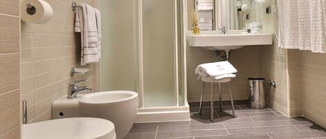 Une salle de bain moderne équipée de toilettes, d’un bidet et d’un lavabo. Elle comprend une douche à parois de verre et un porte-serviettes.