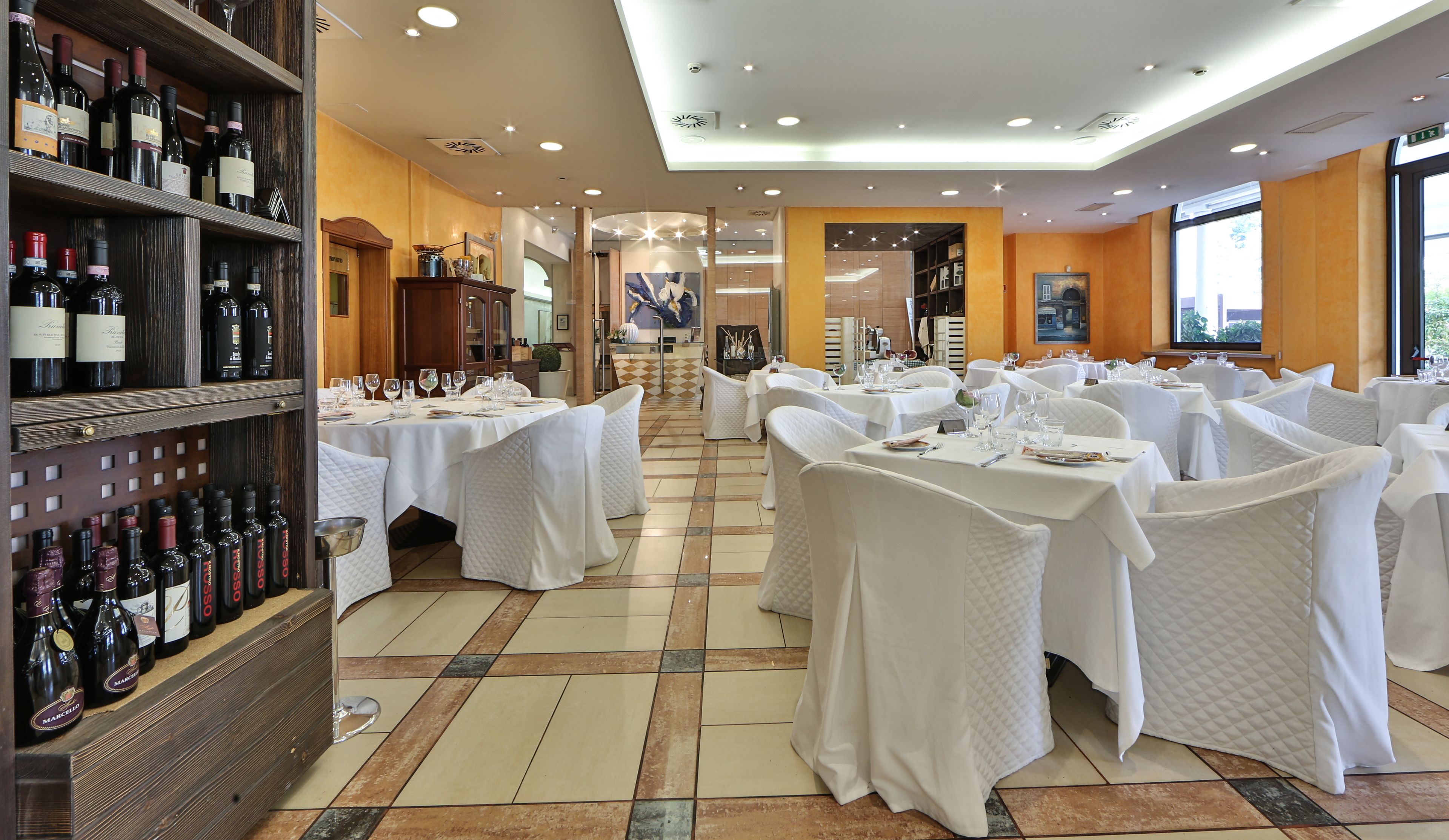 Un ristorante con diversi tavoli, tovaglie bianche e bottiglie di vino sugli scaffali.