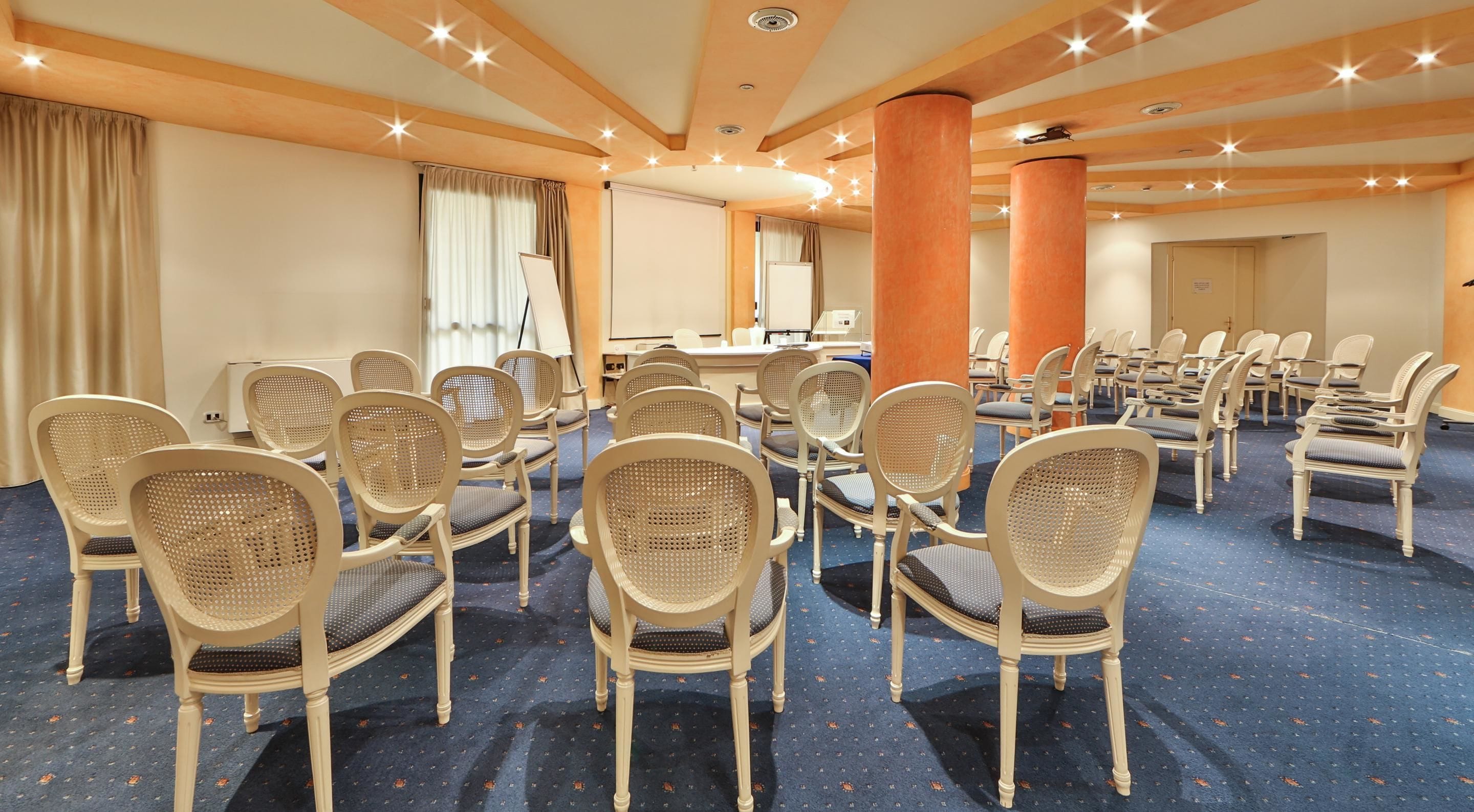 Une salle de conférence avec des rangées de chaises en osier, un écran de projection et une grande table.