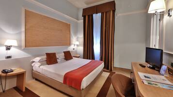 Ein Hotelzimmer mit Bett, Nachttischen, einem Schreibtisch mit Computer und einem Fernseher.